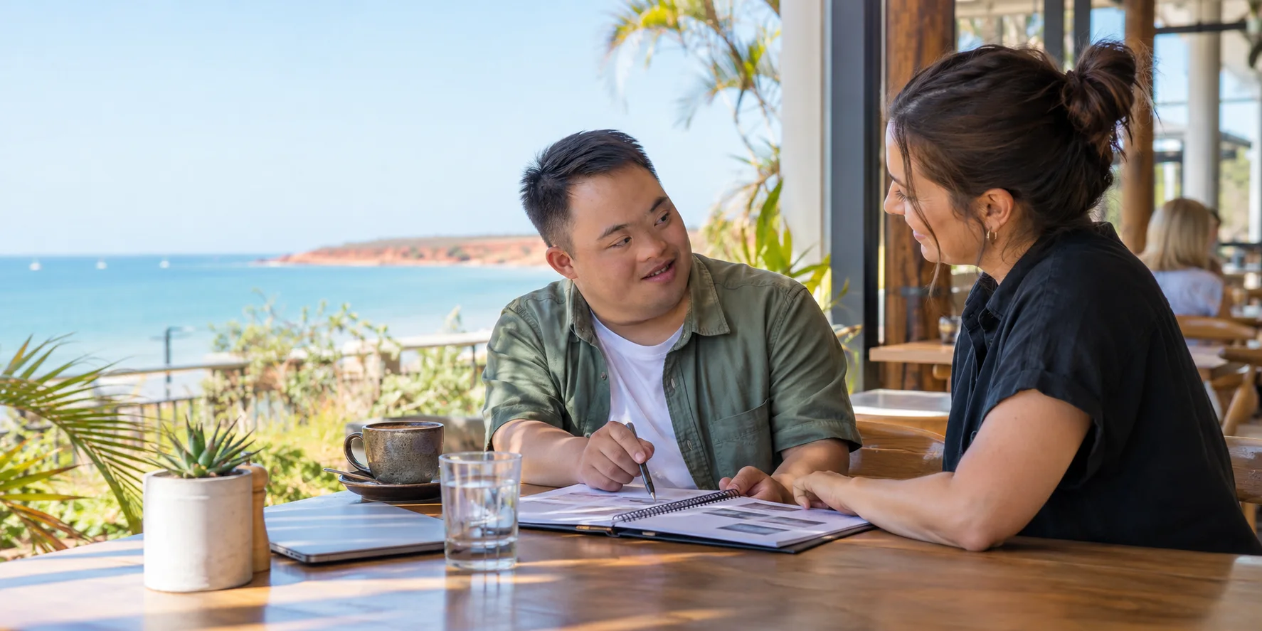 A young man and a practitioner working through a planning folder together at a café table overlooking the ocean