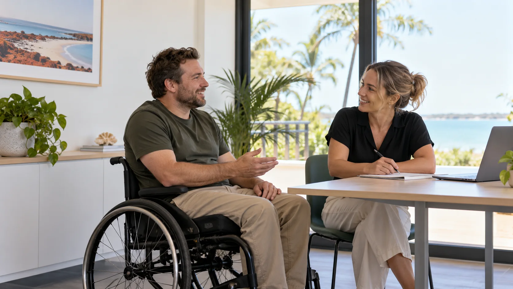 A man in a wheelchair talking and smiling with a practitioner who is taking notes at a table