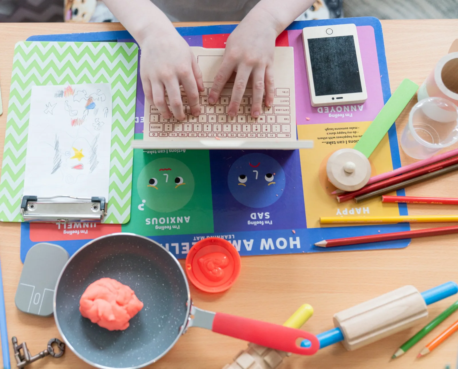 A child typing on a toy keyboard beside a feelings mat showing happy, sad, anxious and annoyed faces