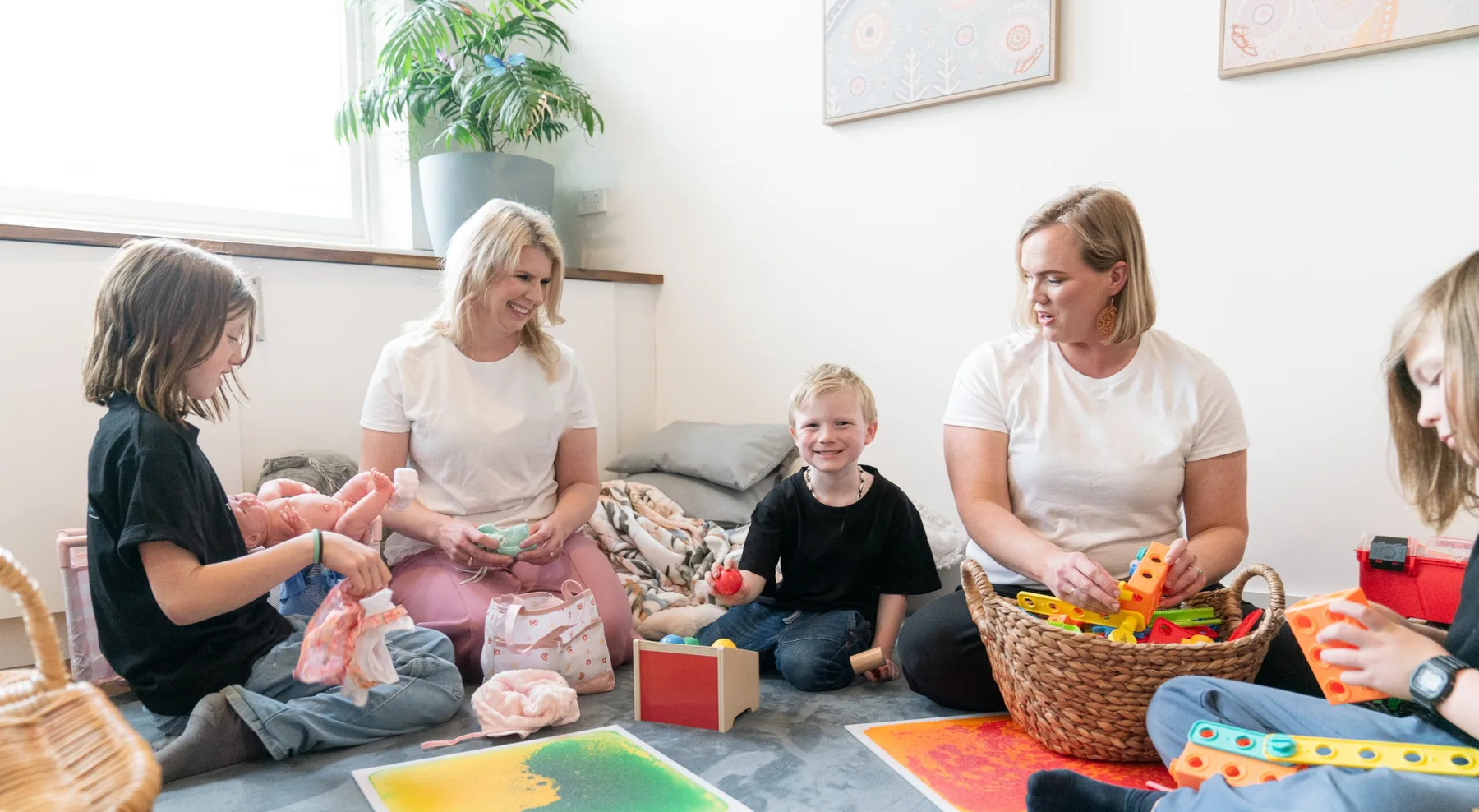 Two practitioners playing with children on the floor of a bright sensory play room