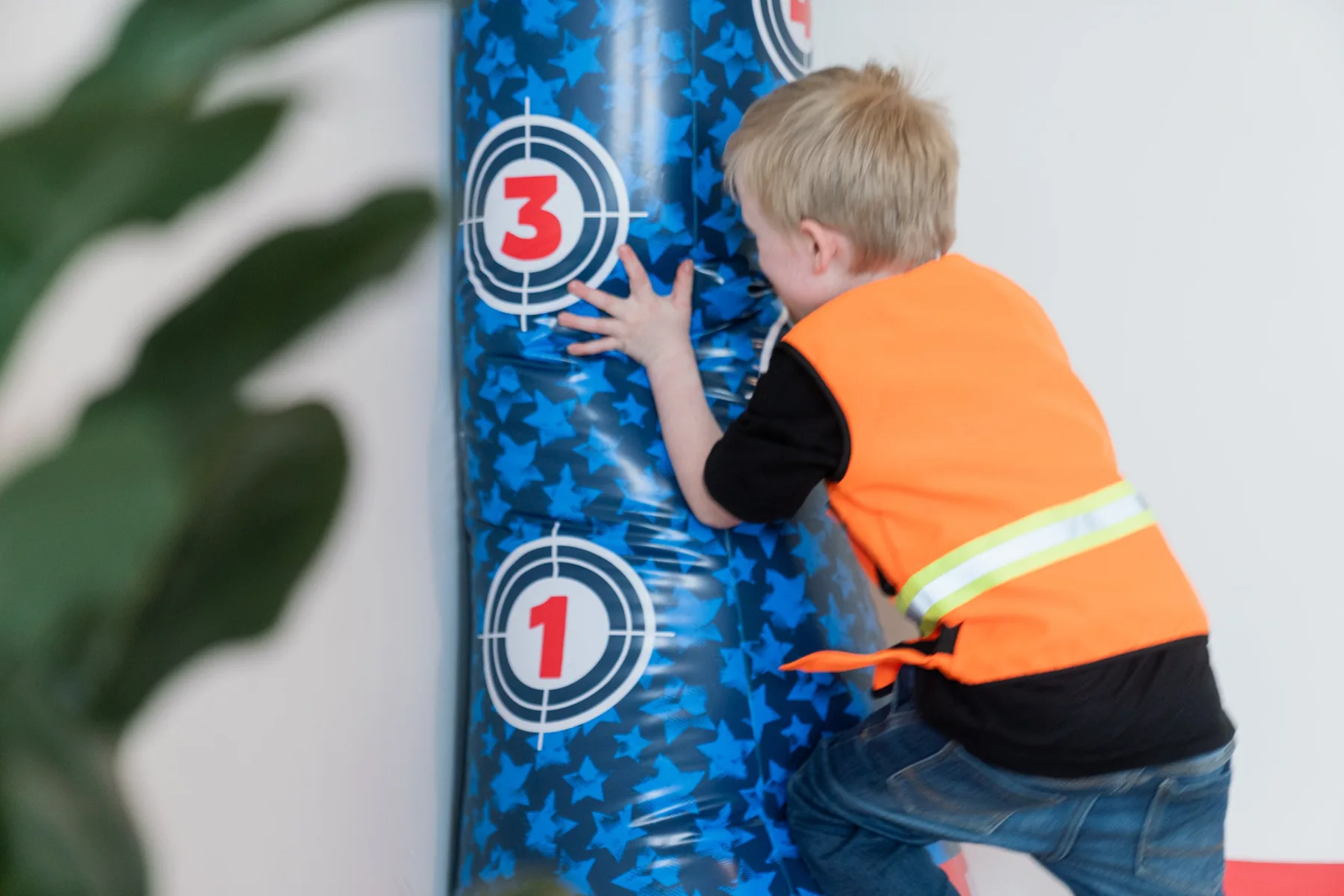 A child in a high-vis vest pushing against a tall inflatable punching bag during a sensory play session